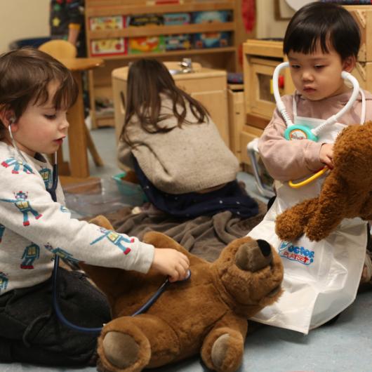 Two children doing role play, pretending to be doctors listening to the teddy's heart