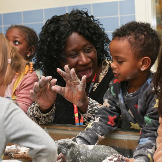 staff and children getting involved in some messy play. Staff's hand full of flour