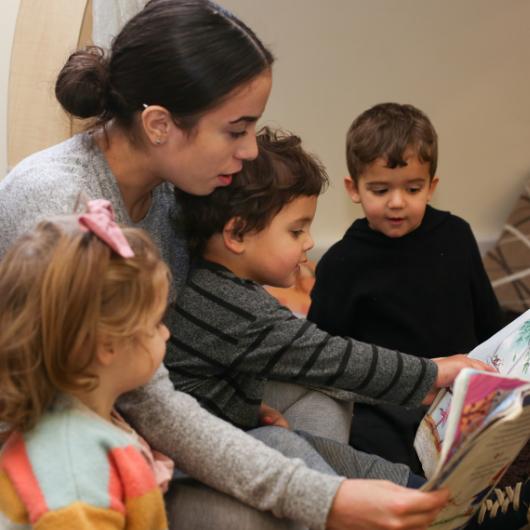 Staff and children sitting down on the carpet reading a book together
