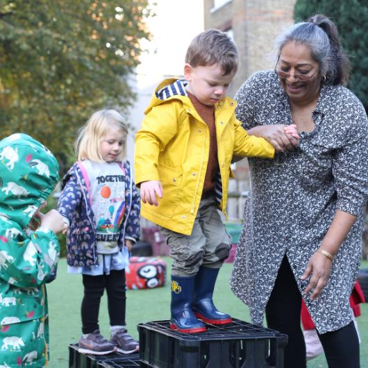 Staff and child outside in the garden practicing risky play and jumping off some crates.