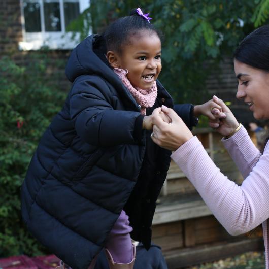 Staff helping a child to jump off something high outside in the garden, practicing risky play and physical activity