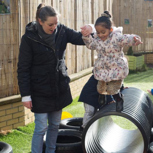 Staff helping a child to jump off something high outside in the garden, practicing risky play and physical activity