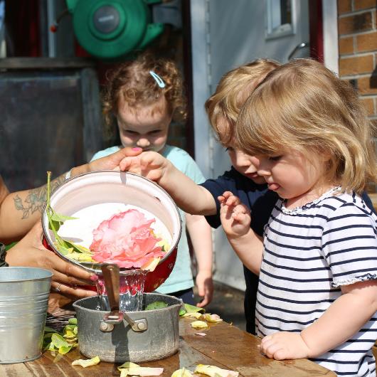 staff and children playing with water, flowers and plants in the home corner outside in the garden.