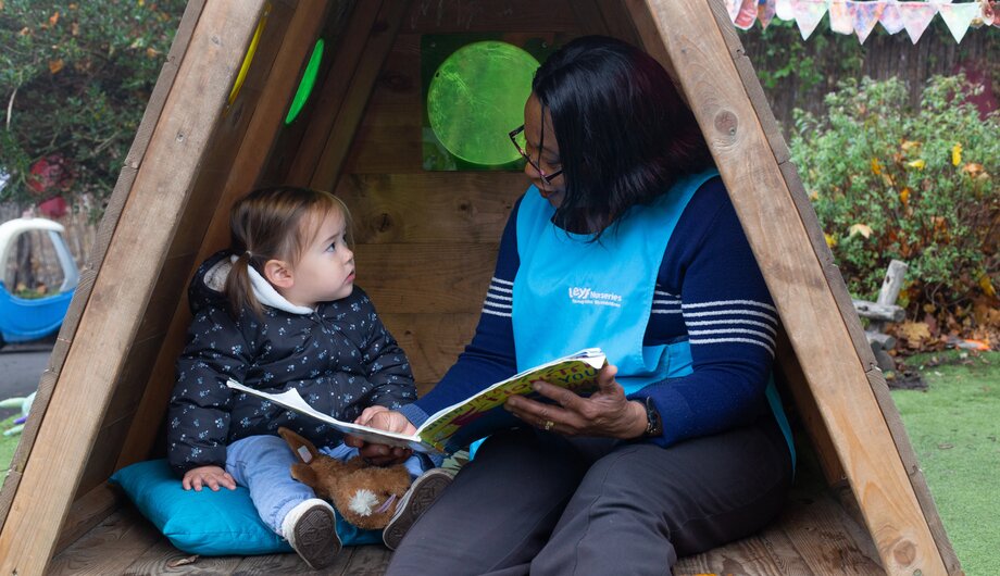 staff and child sitting under wooden tent reading a book
