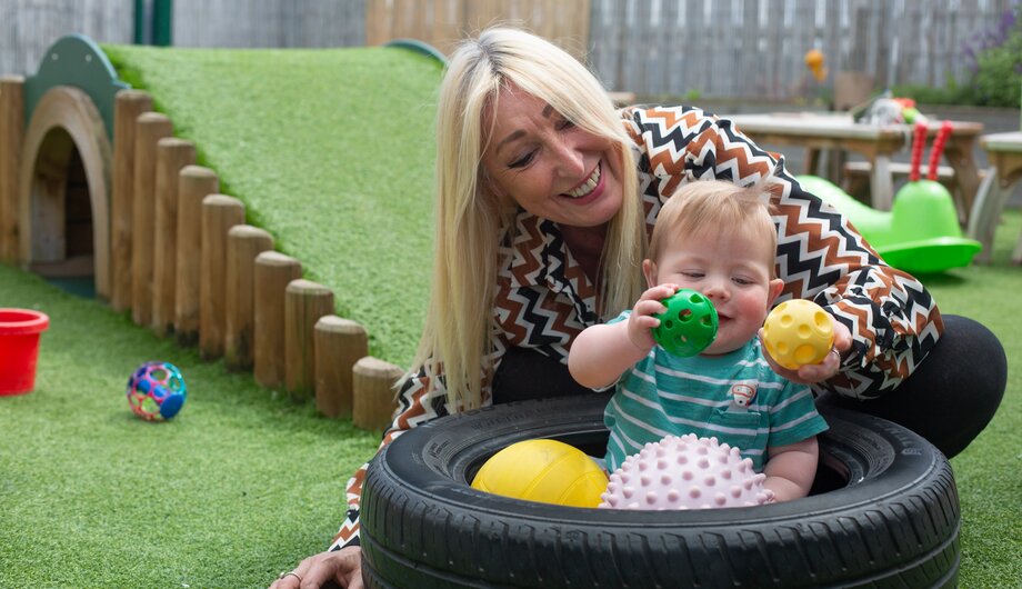 Staff member playing with a baby who is sitting in a ball pit