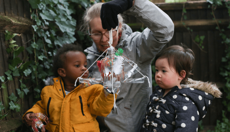 Staff member showing a garden toy made from recycling to two children