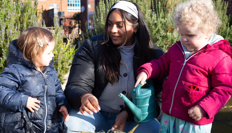 A teacher and children watering and exploring plants.