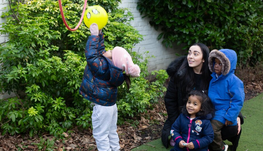 Staff member and child watching another child throwing a ball through a hoop
