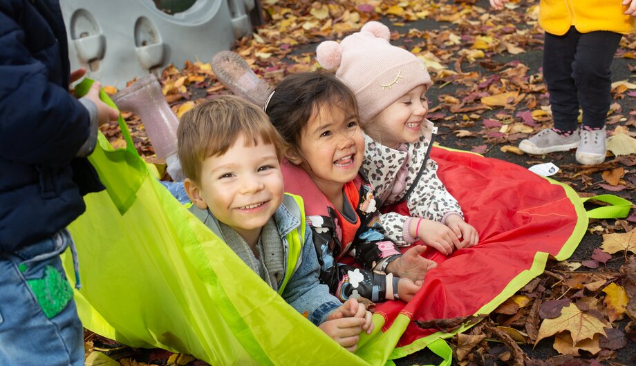 Children laying on a mat with leaves on the ground