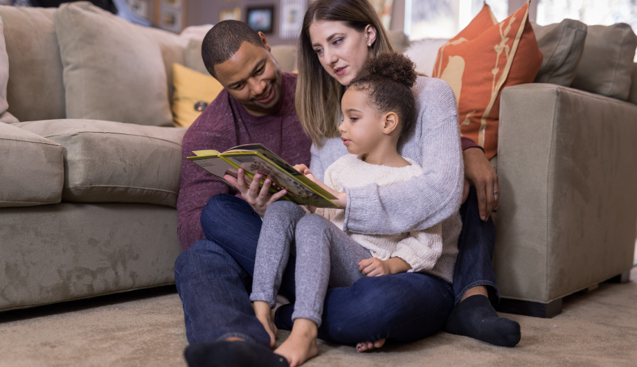 child looking at a book with two adults