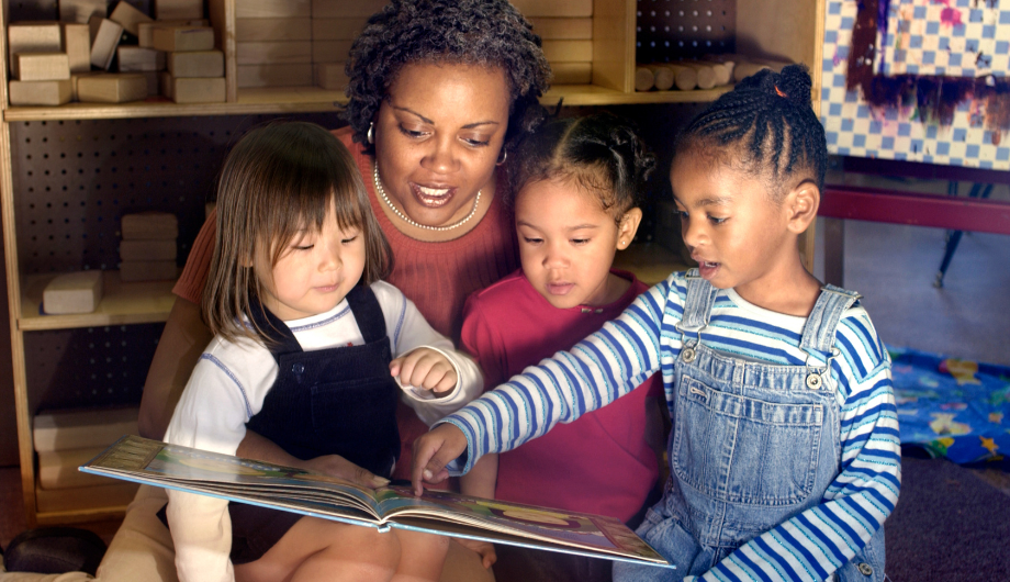 three children looking at a book with an adult