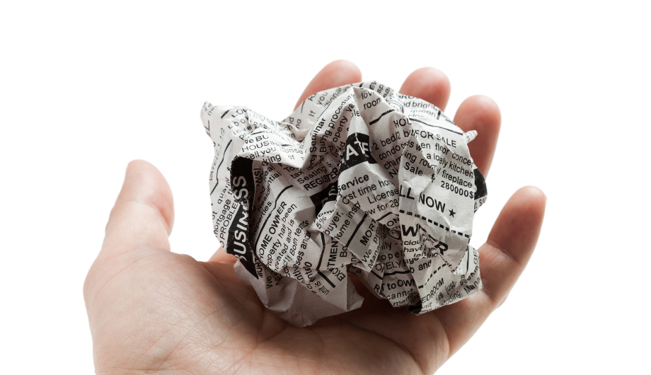 a hand holding a sheet of newspaper rolled in a ball