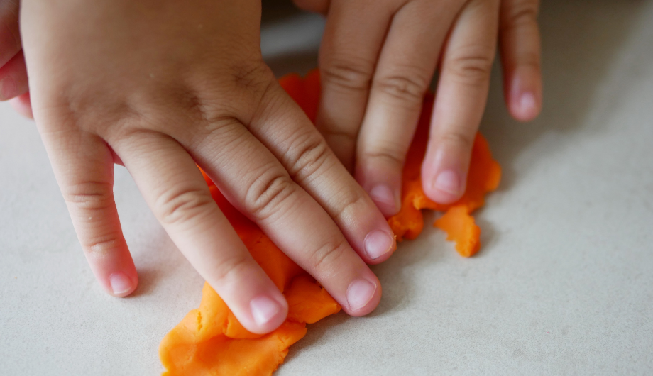 childs hands playing with orange playdough