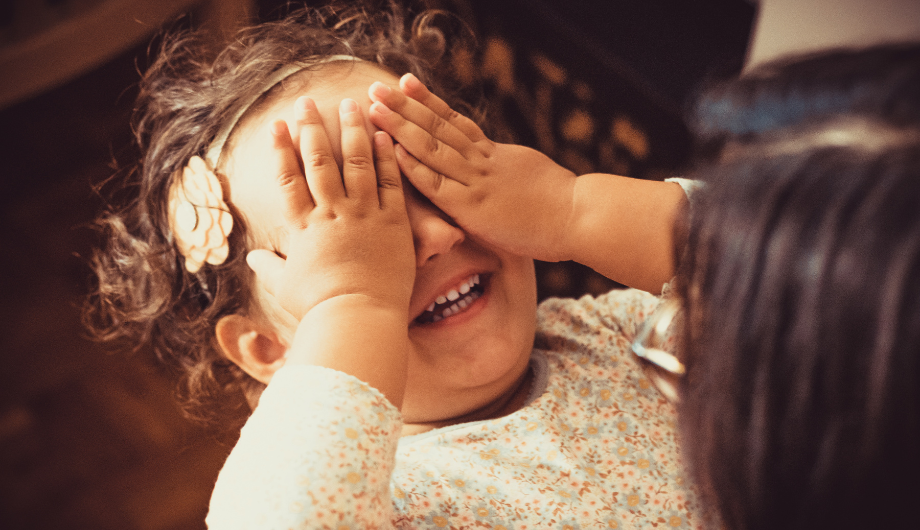 smiling child covering her eyes with her hands