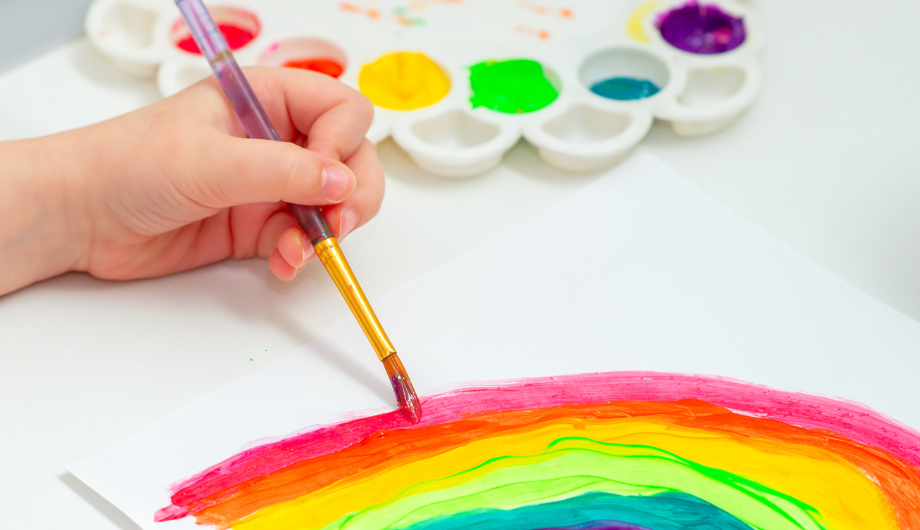 child's hand painting a picture of a rainbow