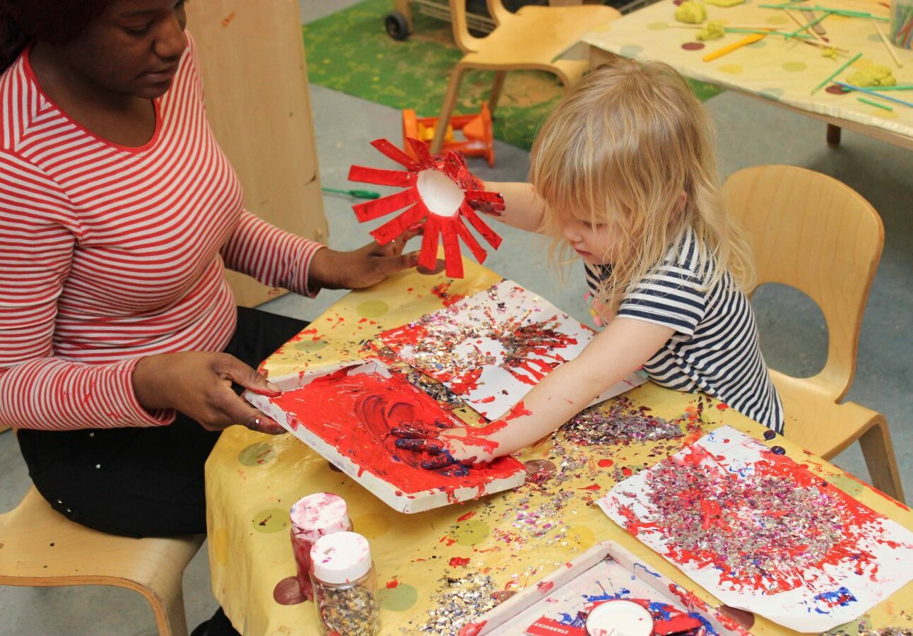 Teacher helping a little girl doing hand painting