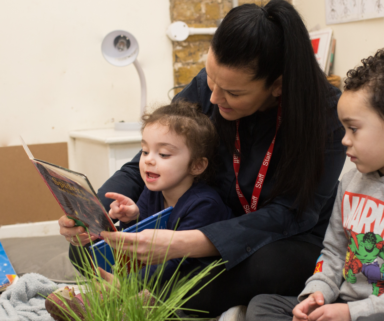 children and staff sitting on the carpet reading a book