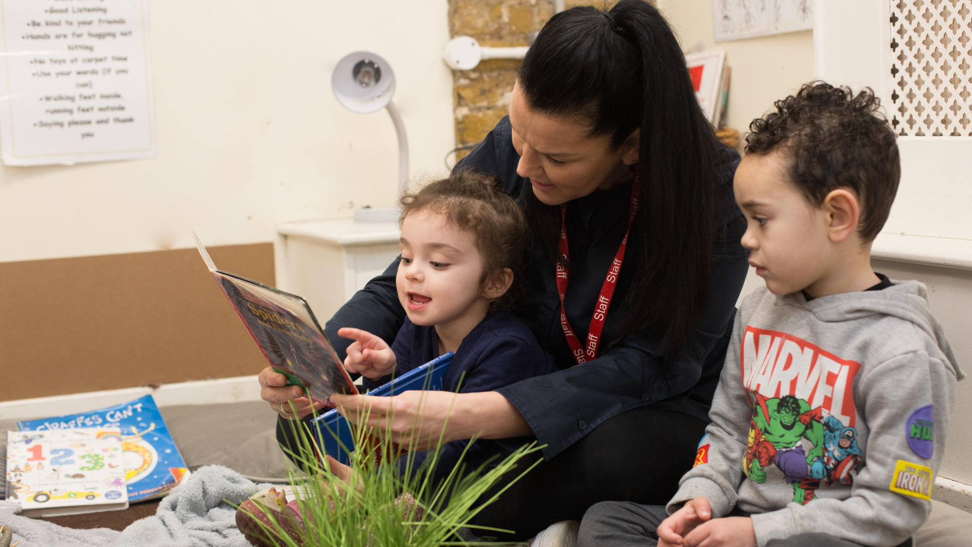 children and staff sitting on the carpet reading a book