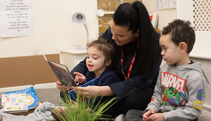 children and staff sitting on the carpet reading a book