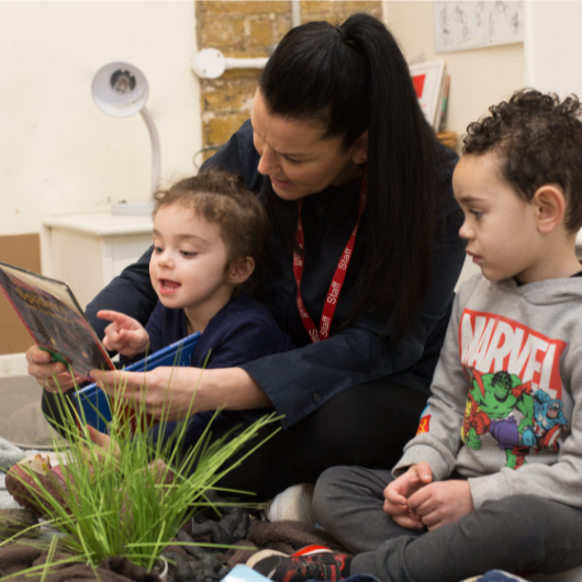 children and staff sitting on the carpet reading a book