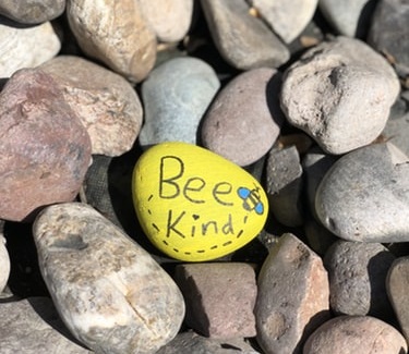 Pebbles, with one painted yellow with the words Bee Kind on it