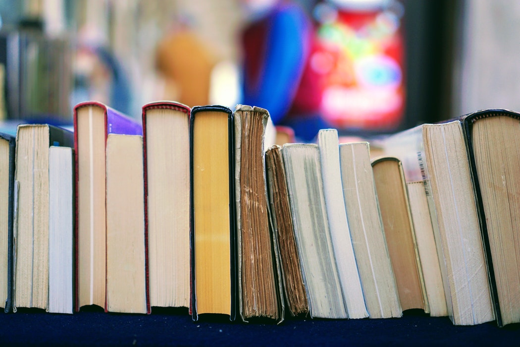 A variety of hardback and paperback books laid on a shelf