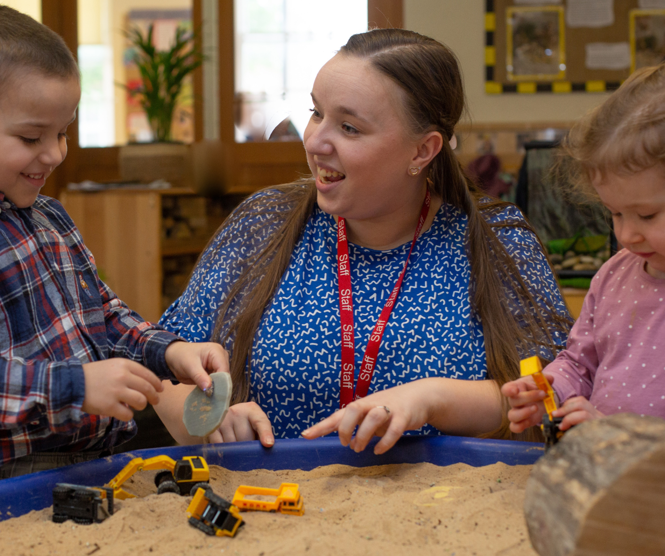 children and staff engaged in an activity using sand and diggers