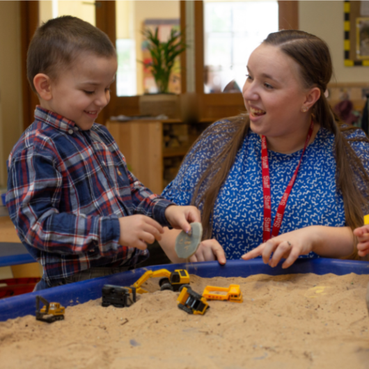 children and staff engaged in an activity using sand and diggers