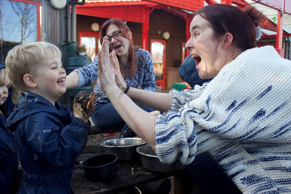 Teachers and children outdoors showing each other their muddy hands