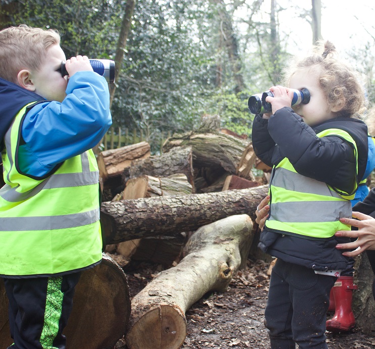 Two children in high vis vests looking at each other through binoculars