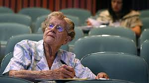 An elderly lady in a lecture theatre taking notes