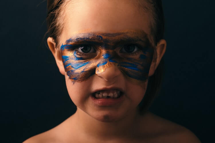 Grimacing child with blue and gold face paint around their eyes