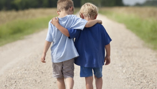 View of two boys seen from behind walking with their arms around each others shoulders