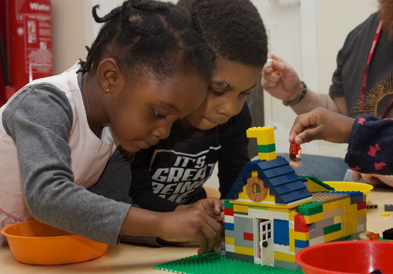 Two children playing with a lego model of a house