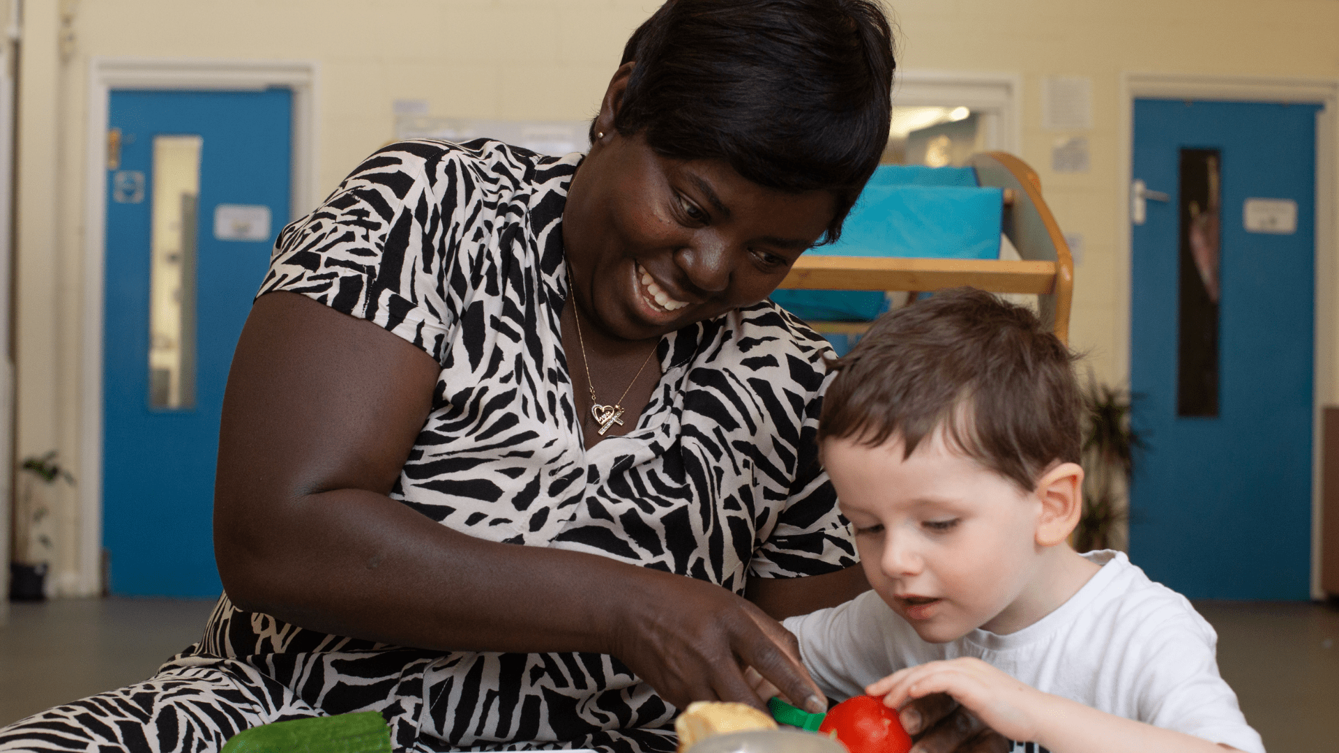 Member of staff helping the child cut some vegetables in the home corner