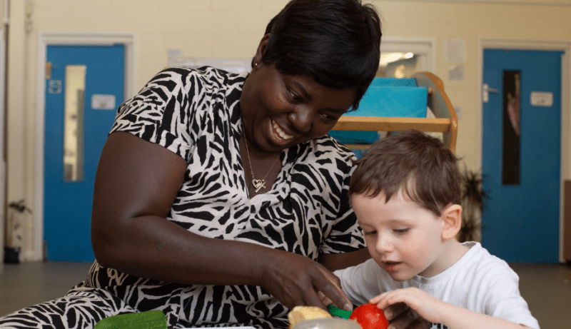 Member of staff helping the child cut some vegetables in the home corner