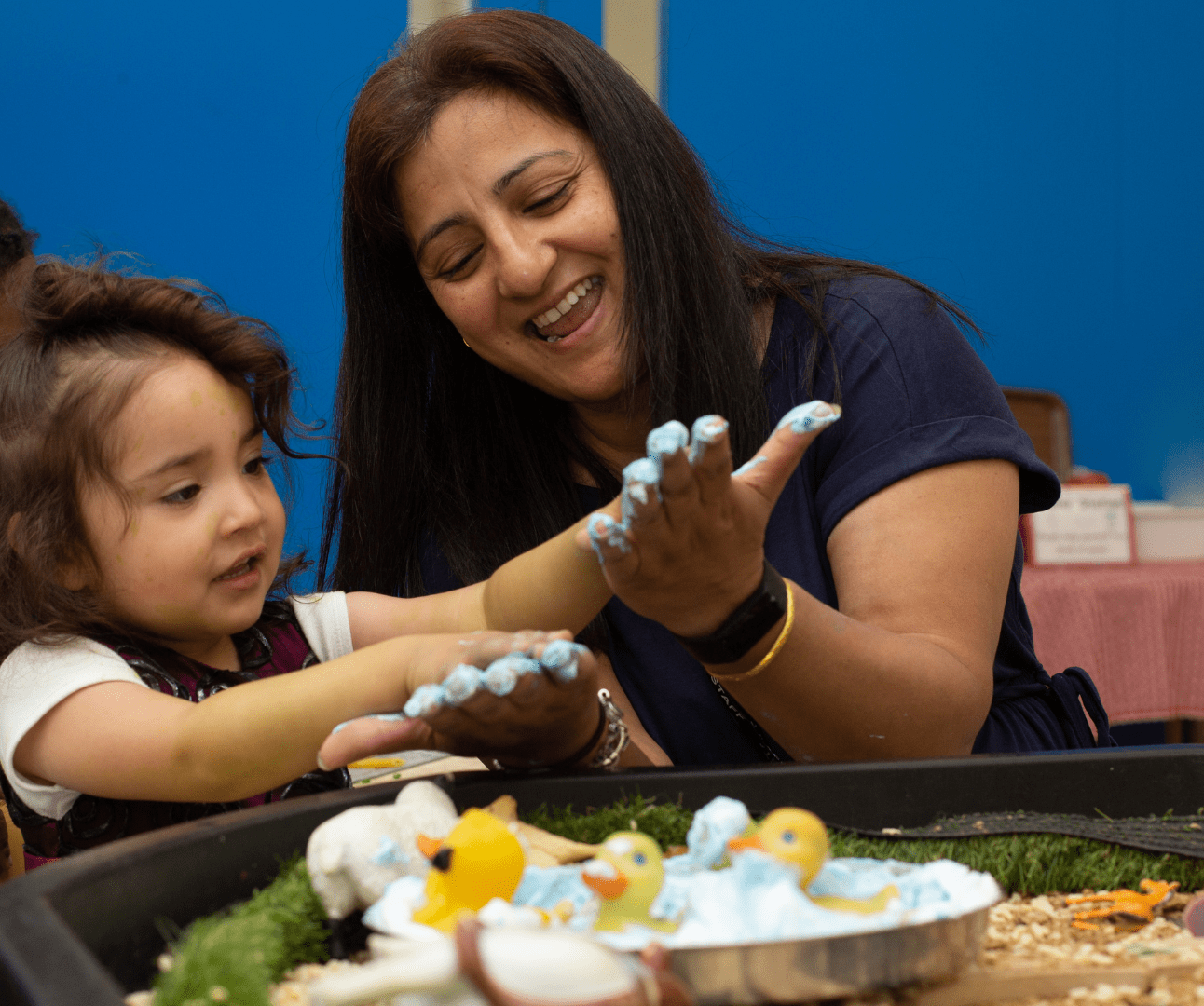 staff and child enjoying messy play with paint on their hands