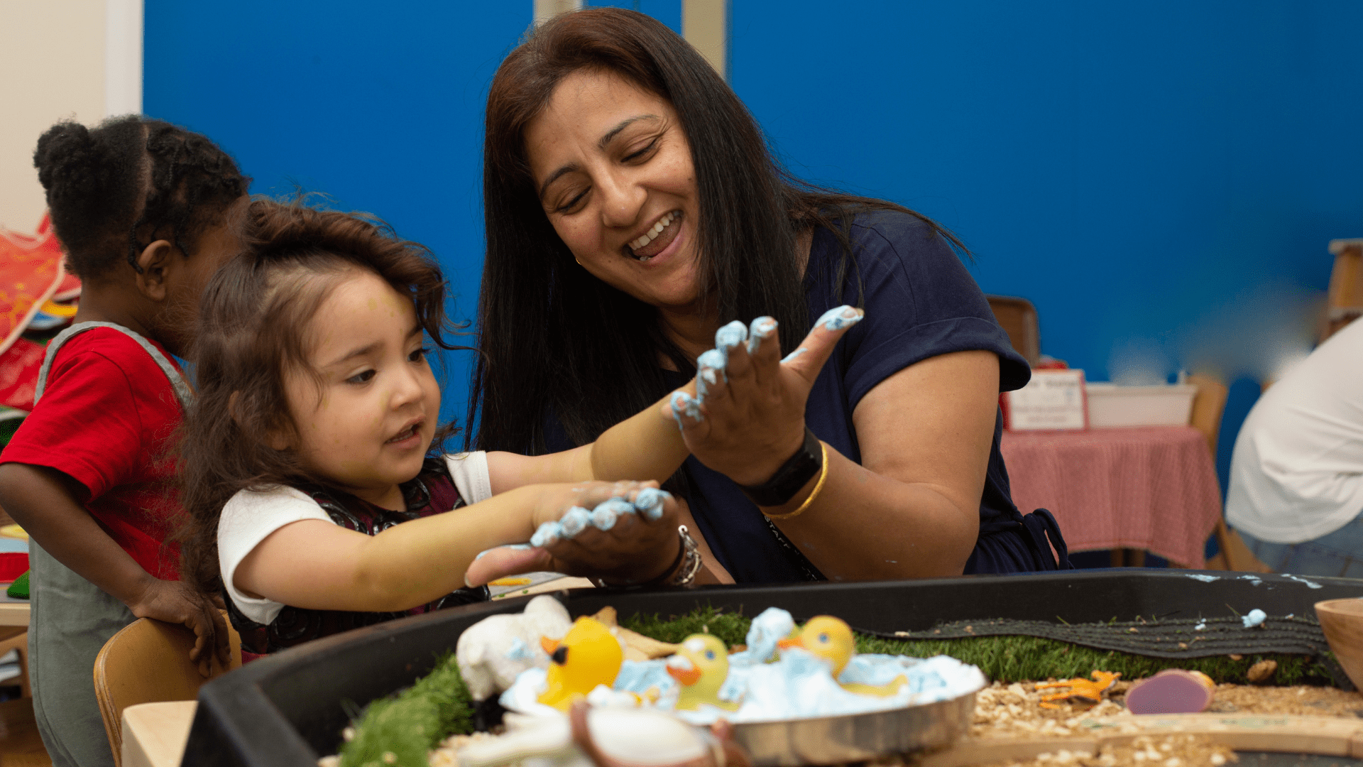 staff and child enjoying messy play with paint on their hands