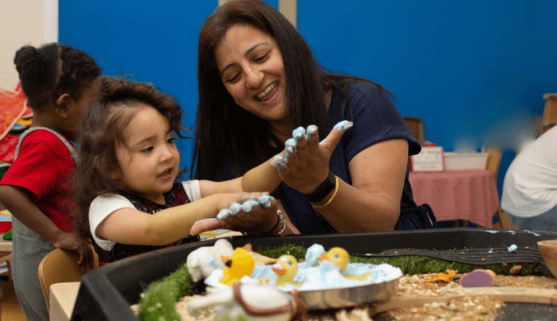 staff and child enjoying messy play with paint on their hands