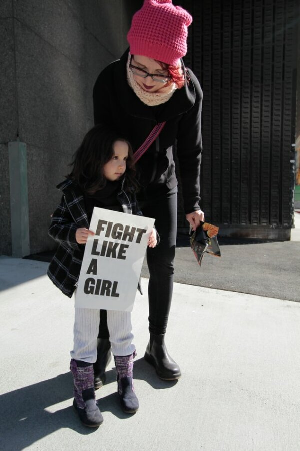 Woman standing next to a little girl holding a poster which says 'Fight like a girl'