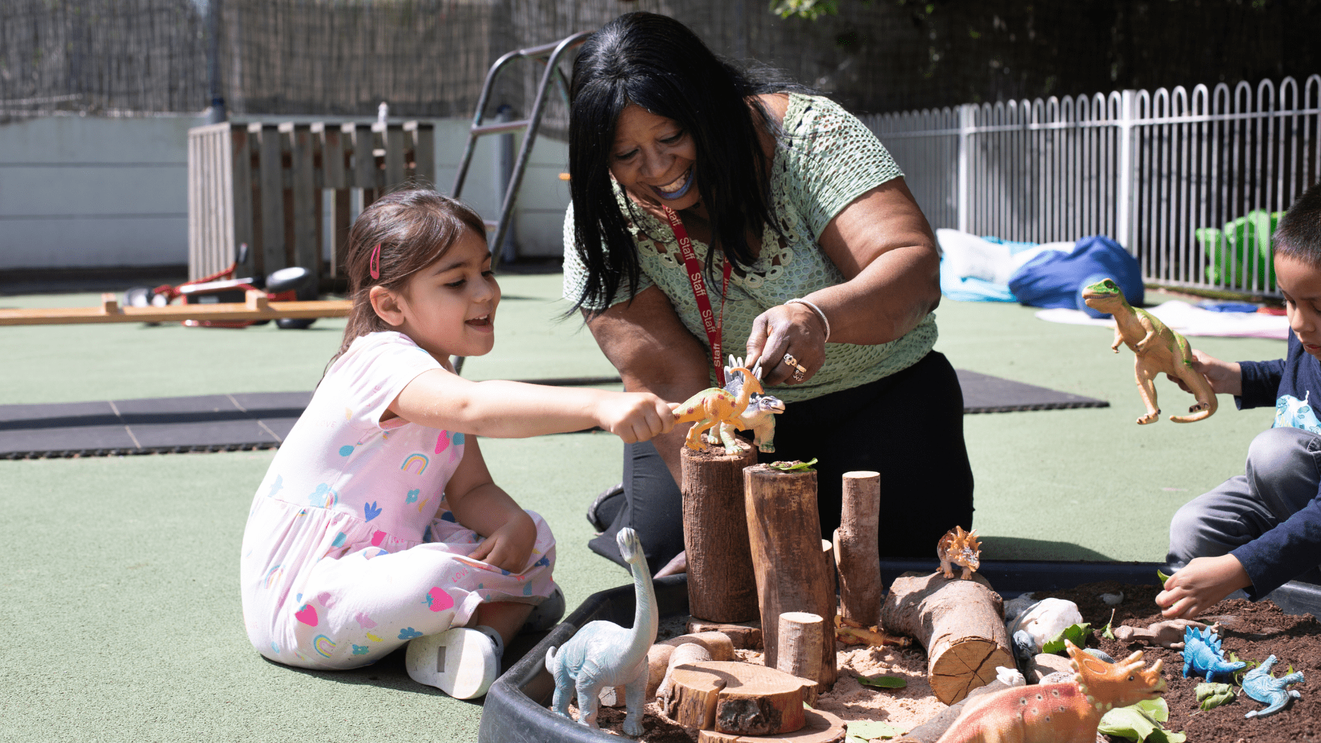 staff and child playing with dinosaurs outside in the garden