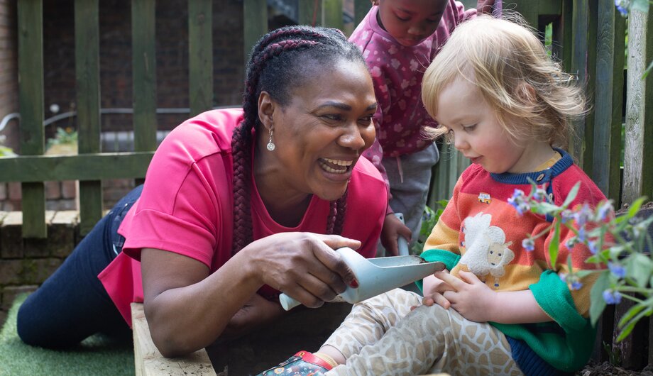 Nursery staff member and two small children doing gardening with trowels