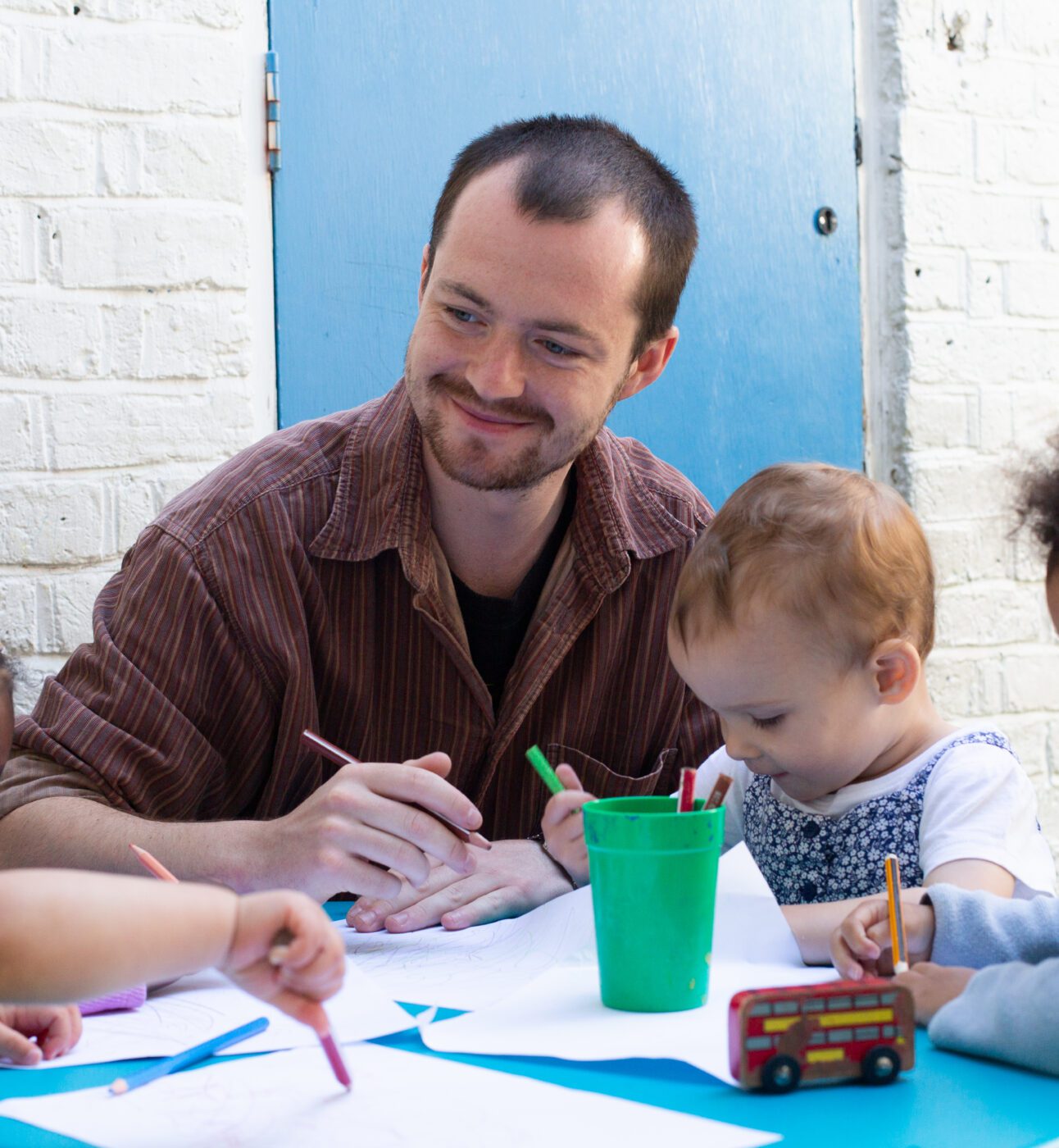 A male teacher helping a group of children with a drawing activity