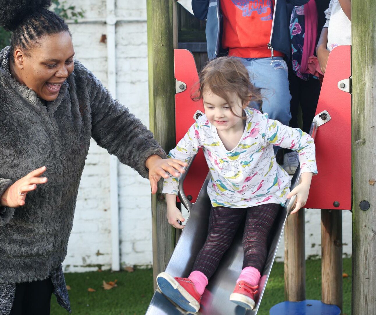 Child going down a slide with staff member helping