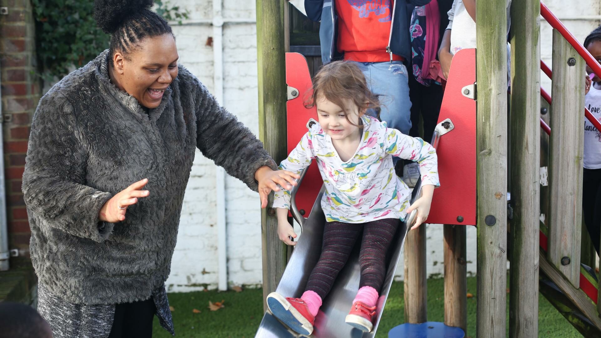 Child going down a slide with staff member helping