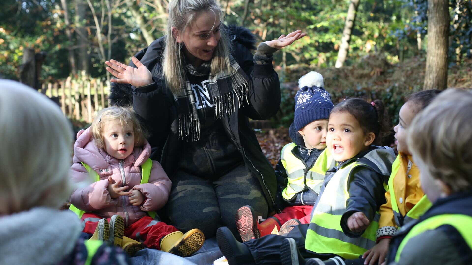 Staff and a group of children sitting down at their local park engaging in an activity.