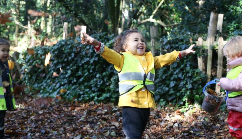 Child at the local park enjoying the forest school and throwing leaves in the air