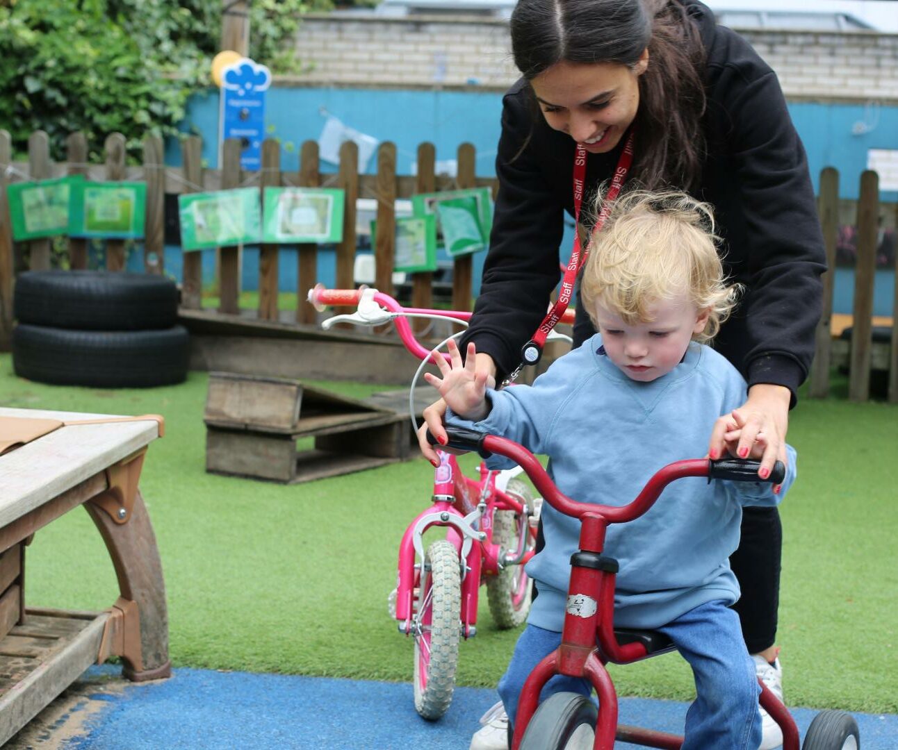 Child riding a bike with staff member holding handlebars