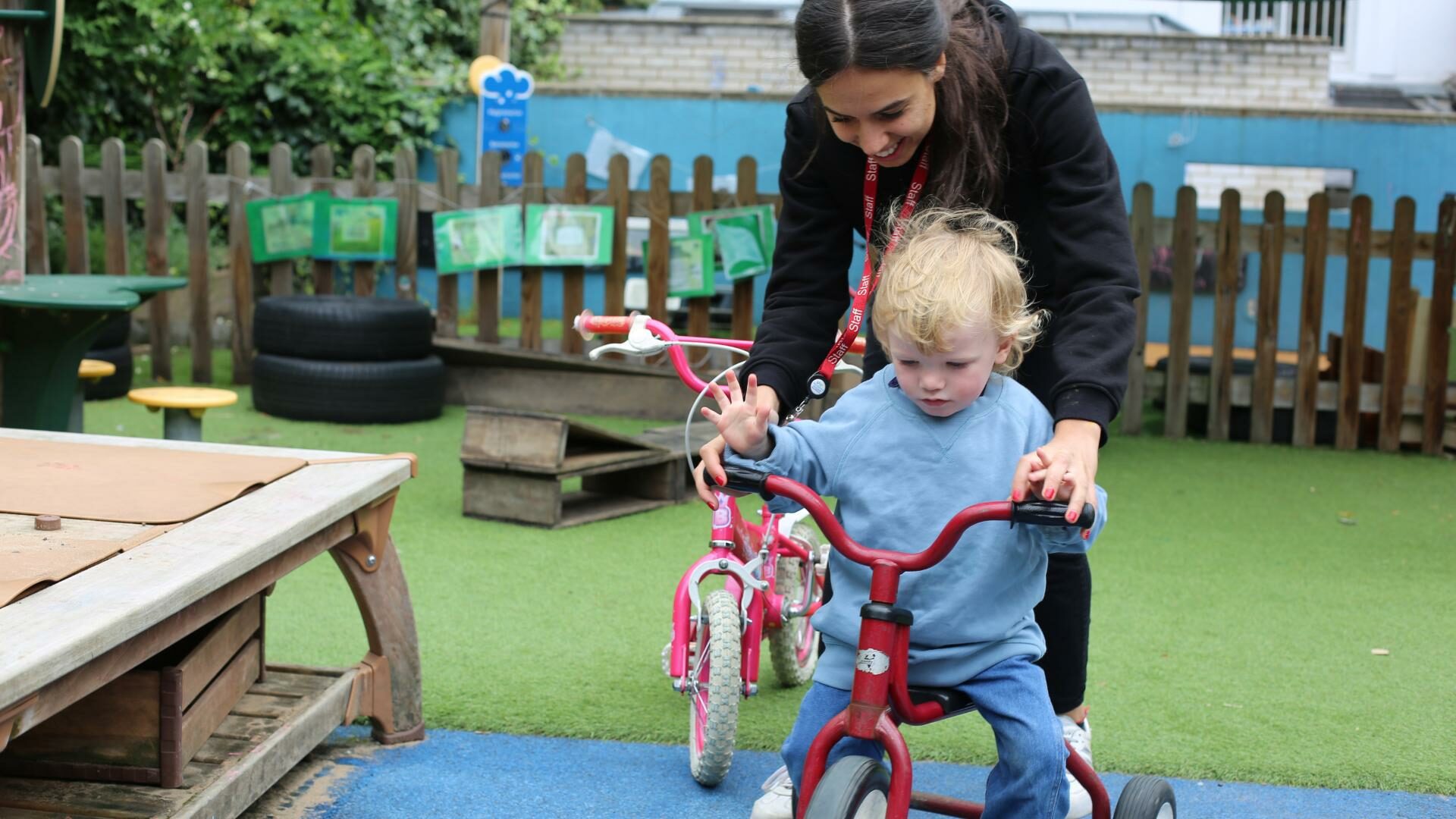 Child riding a bike with staff member holding handlebars