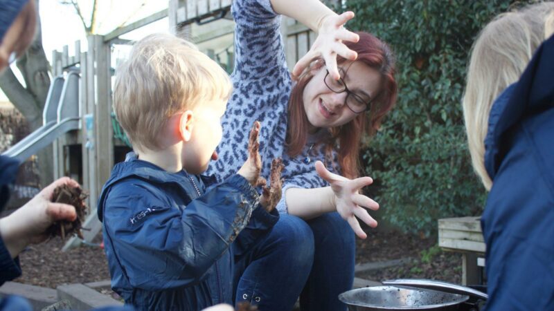 Staff and child showing each other their muddy hands